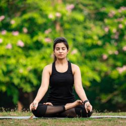 Young Asian/ Indian woman wearing black sports dress and meditating outdoors at park.